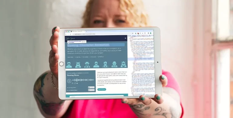 Helen Bee from B Double E holding an ipadout in front of her with a website showing an h tag guide. The ipad covers most of her face, she's wearing a bright pink t-shirt and stood infront of a white brick wall.